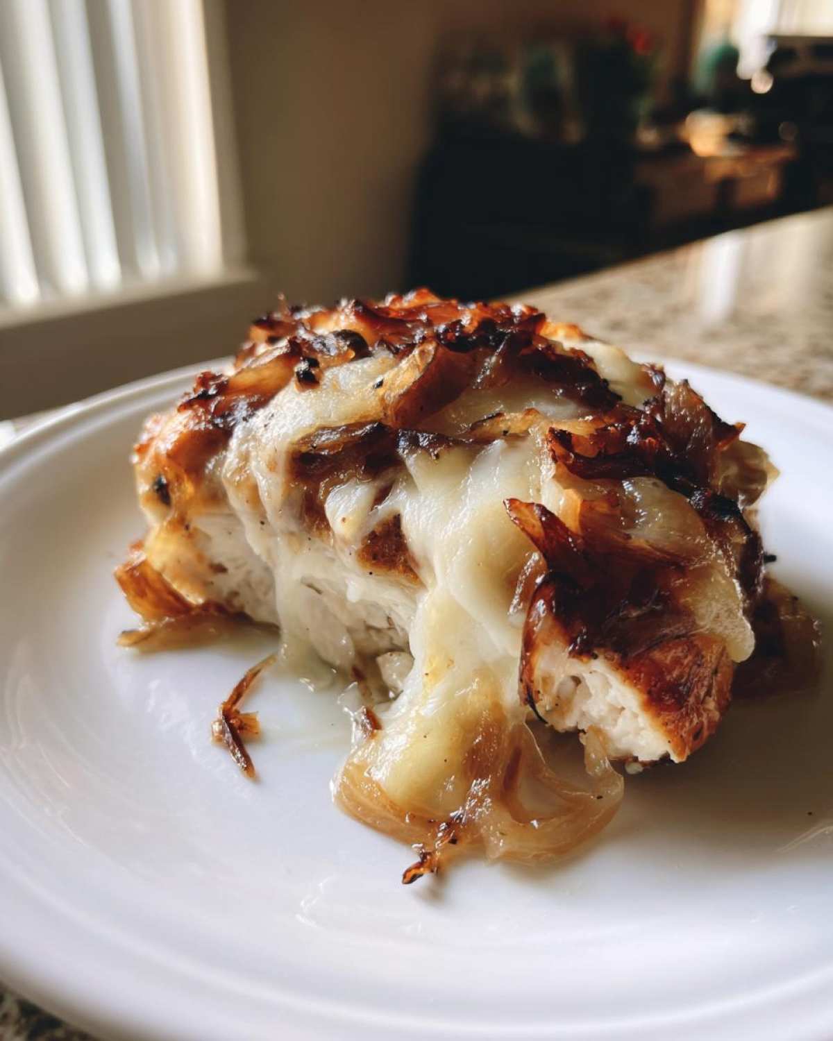 Close-up of a juicy french onion chicken breast topped with melted white cheese and caramelized onions.
