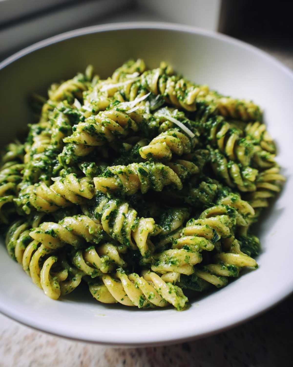 A close-up shot of fusilli pasta thoroughly coated in vibrant green pesto pasta sauce, topped with grated cheese.