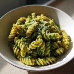 Close-up of spiral fusilli pesto pasta generously coated in green sauce and topped with grated cheese.