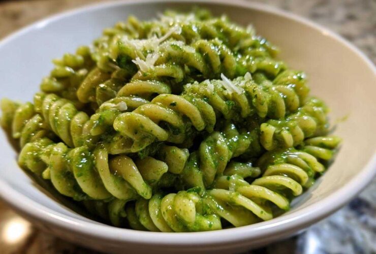 A close-up shot of vibrant green pesto pasta, made with fusilli noodles, topped with grated Parmesan cheese.
