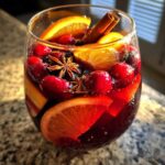 Close-up of a glass filled with vibrant Christmas sangria, featuring orange slices, cranberries, star anise, and a cinnamon stick.
