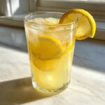 A tall, chilled glass filled with homemade lemonade, ice cubes, and garnished with fresh lemon slices.