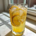 Close-up of a tall glass filled with fizzy, yellow lemonade, ice, and fresh lemon slices.