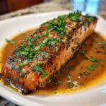 A perfectly cooked, glazed salmon fillet topped with fresh parsley, resting in a rich brown sauce.