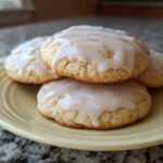 Close-up of four soft, glazed sugar cookies stacked slightly on a pale yellow plate.