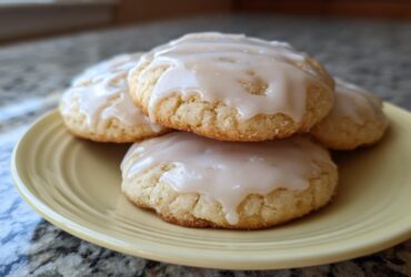 Close-up of four soft, glazed sugar cookies stacked slightly on a pale yellow plate.