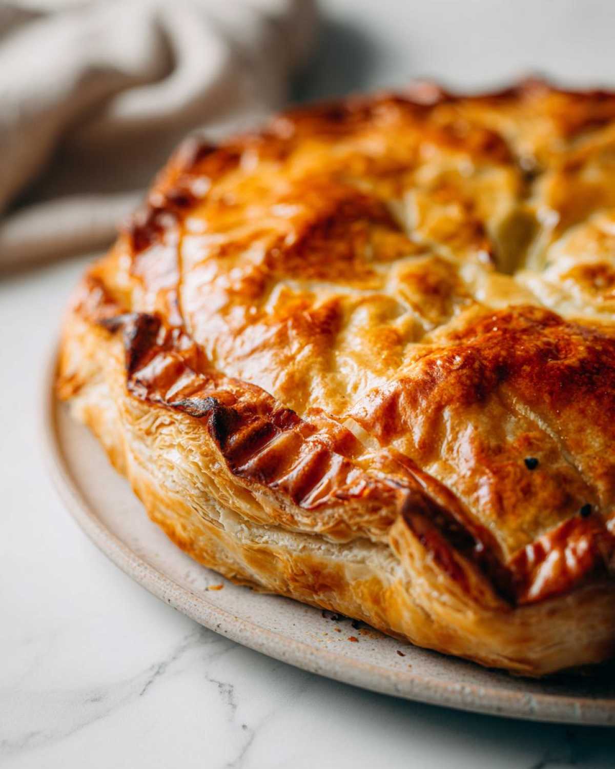 Close-up of a perfectly golden brown baked brie in puff pastry with flaky layers.