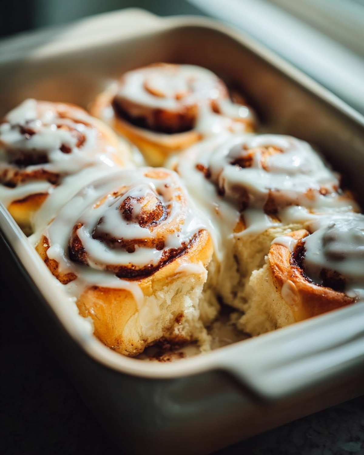 Close-up of gooey small batch cinnamon rolls topped with white icing in a baking dish.