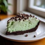 A close-up slice of light green grasshopper pie with a dark chocolate crust, topped with mini chocolate chips.