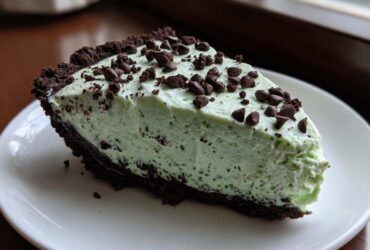 A close-up of a creamy, light green slice of grasshopper pie with a dark chocolate crust, topped with chocolate chips.
