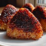 Four golden-brown, triangular grilled rice balls with a dark, caramelized crust served on a white plate.