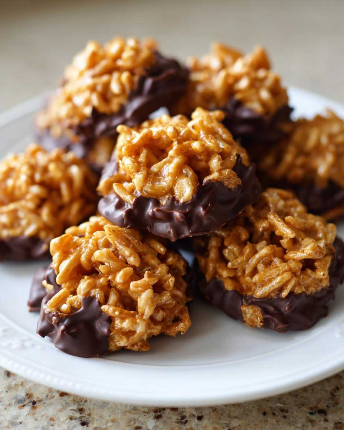 A pile of golden brown haystack cookies dipped in dark chocolate resting on a white plate.