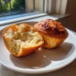 A homemade english muffin, split open to show the fluffy interior, sitting next to the other half on a white plate.