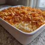 A freshly baked hot chicken salad casserole in a white baking dish, topped generously with golden, crunchy cornflakes.