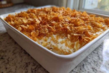 A freshly baked hot chicken salad casserole in a white baking dish, topped generously with golden, crunchy cornflakes.