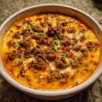 Close-up of a bubbling hot sausage cream cheese dip topped with browned sausage crumbles and green onions.