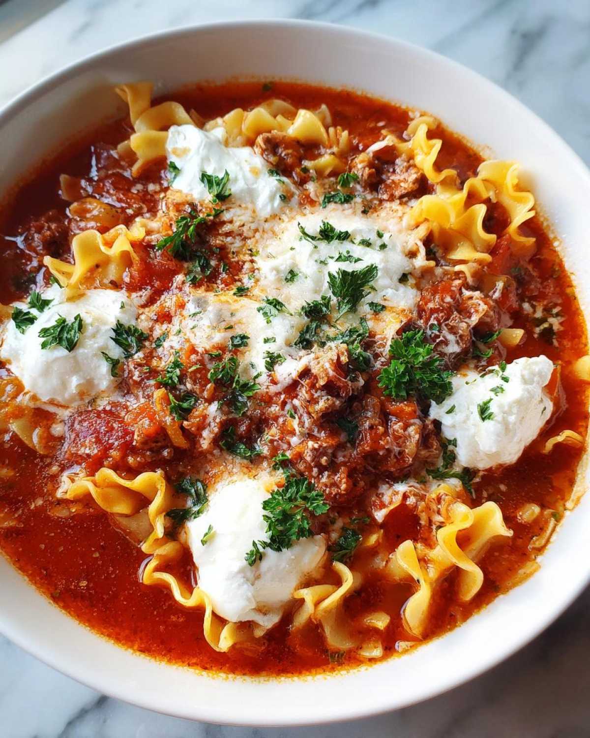 Close-up of a hearty bowl of instant pot lasagna soup topped with dollops of ricotta cheese and fresh parsley.