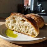 Cross-section of crusty Italian bread showing an open, airy crumb, served with olive oil on a speckled plate.