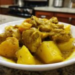 A close-up of tender pieces of Jamaican curry chicken served with large chunks of yellow potatoes in a rich, savory sauce.