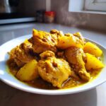 Close-up of hot, steaming Jamaican Curry Chicken served with large chunks of yellow potato on a white plate.