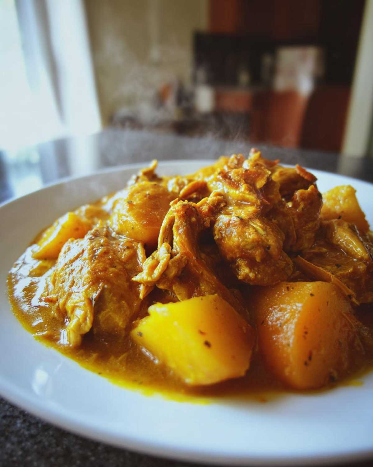 Close-up of hot Jamaican curry chicken pieces served with large chunks of yellow potatoes in a rich curry sauce.