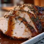 Close-up of sliced, juicy instant pot turkey breast, seasoned with herbs and drizzled with brown gravy.