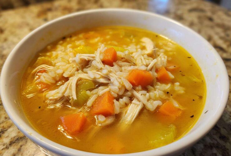 Close-up of a white bowl filled with vibrant Lemon Ginger Turmeric Chicken and Rice Soup, showing shredded chicken, rice, carrots, and celery.