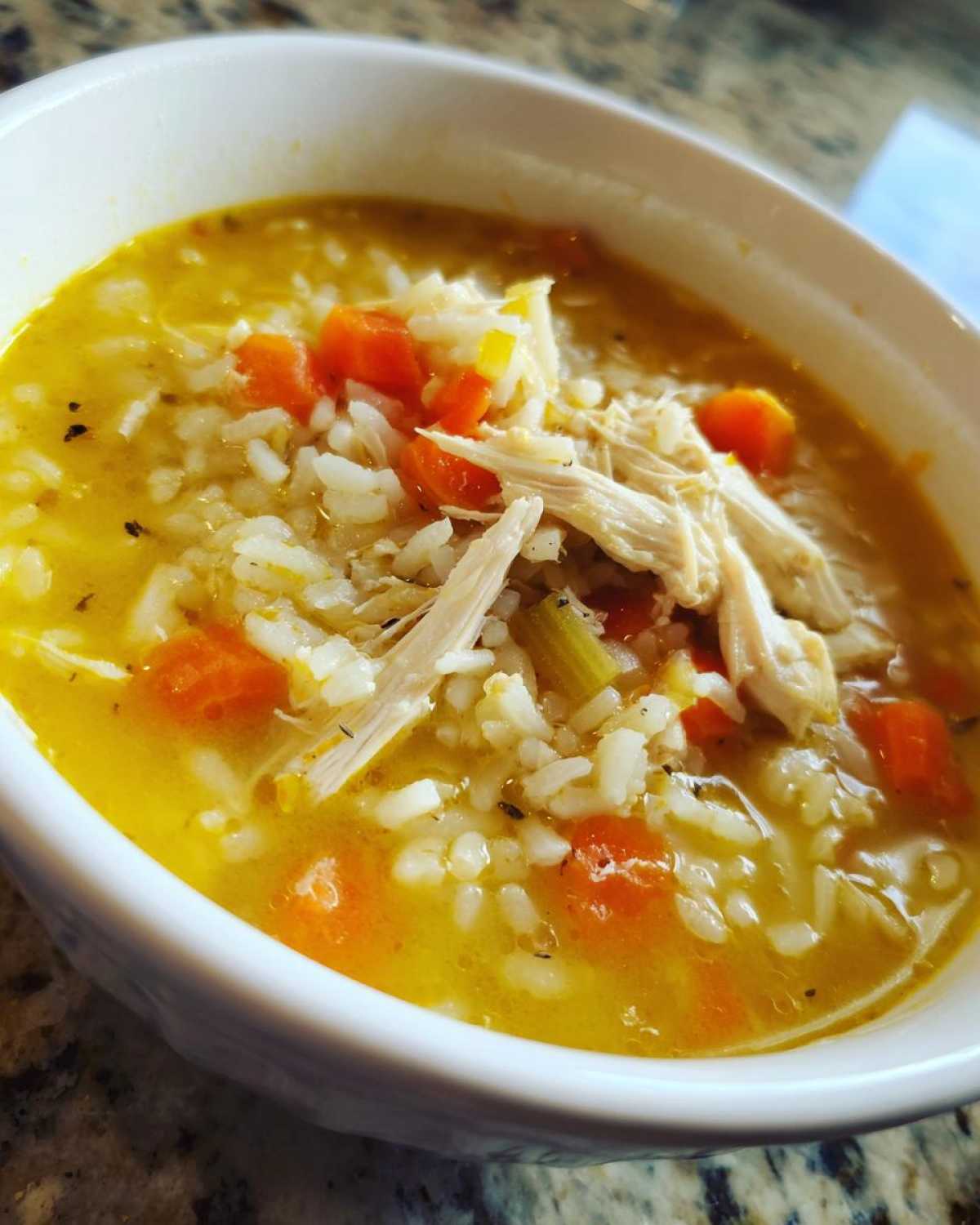 Close-up of a white bowl filled with vibrant yellow Lemon Ginger Turmeric Chicken and Rice Soup, showing shredded chicken, rice, and carrots.