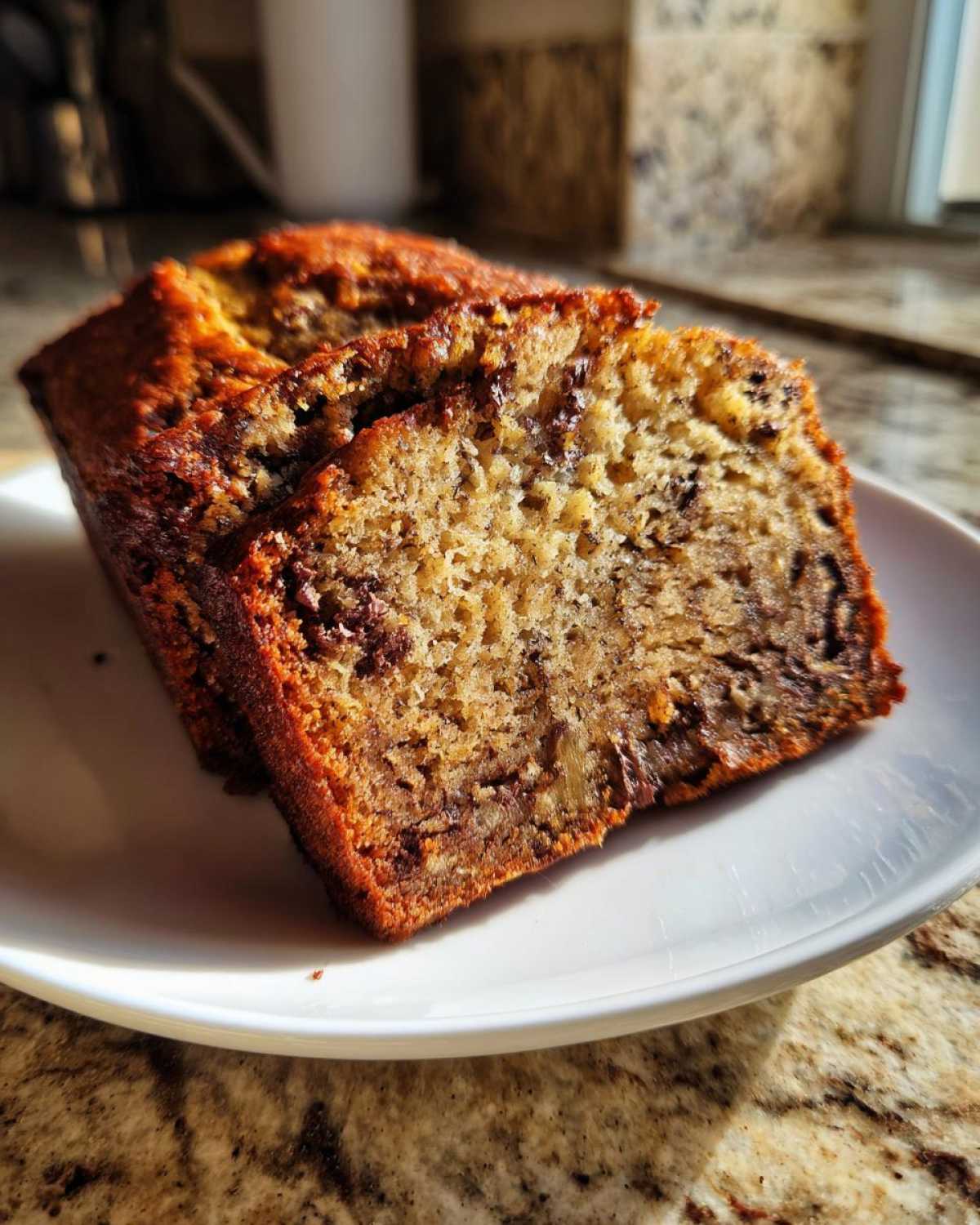 Two thick slices of moist vegan banana bread with visible chocolate chips resting on a white plate.