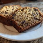 Two thick slices of moist vegan banana bread studded with chocolate chips, served on a white plate.