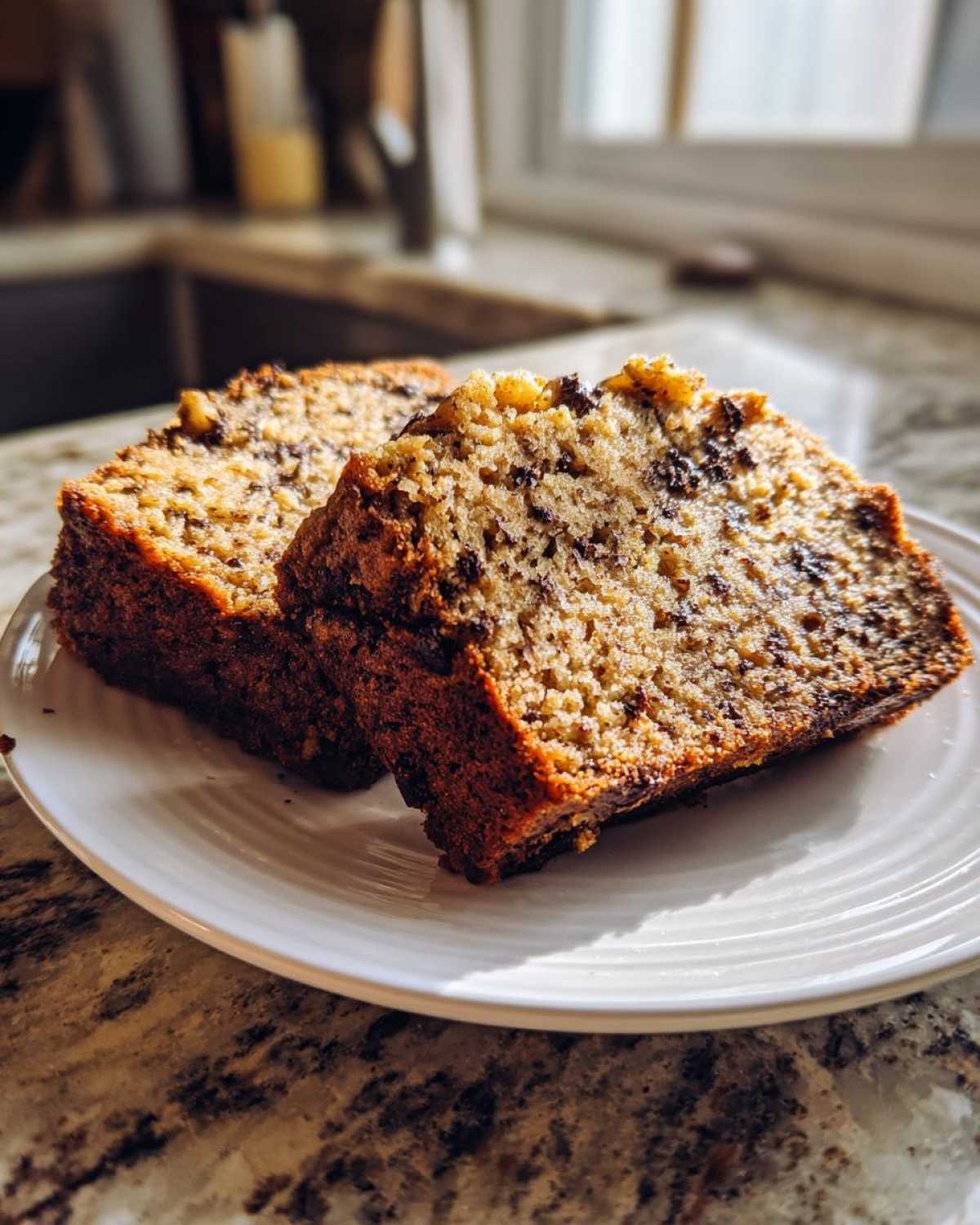 Two thick, moist slices of vegan banana bread studded with chocolate chips on a white plate.