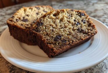 Two thick slices of moist vegan banana bread studded with chocolate chips, served on a white plate.