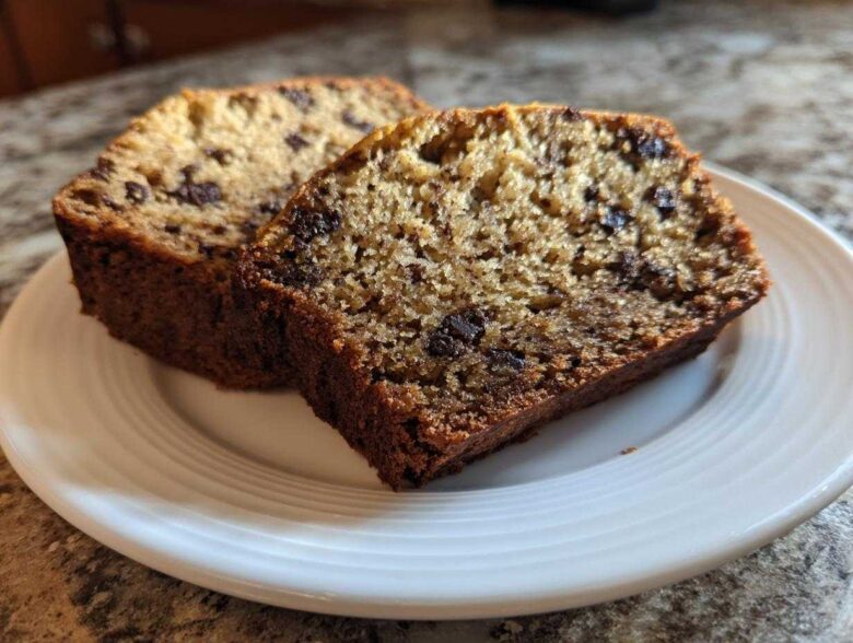 Two thick slices of moist vegan banana bread studded with chocolate chips, served on a white plate.