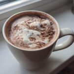 Close-up of a white mug filled with rich hot cocoa mix topped with melted marshmallows or whipped cream.