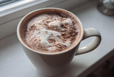 Close-up of a white mug filled with rich hot cocoa mix topped with melted marshmallows or whipped cream.