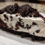 A thick slice of creamy, no-bake Oreo cheesecake featuring a dark chocolate crust and topped with crushed Oreos.