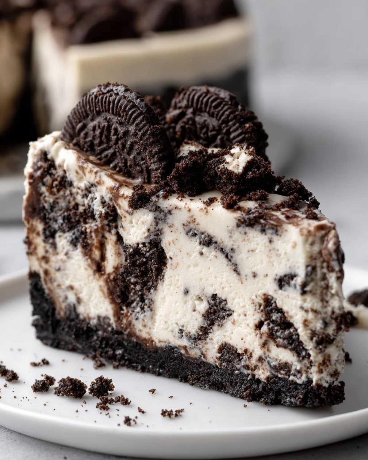 A decadent slice of Oreo cheesecake featuring a dark cookie crust, creamy filling swirled with chocolate, and topped with Oreo pieces.