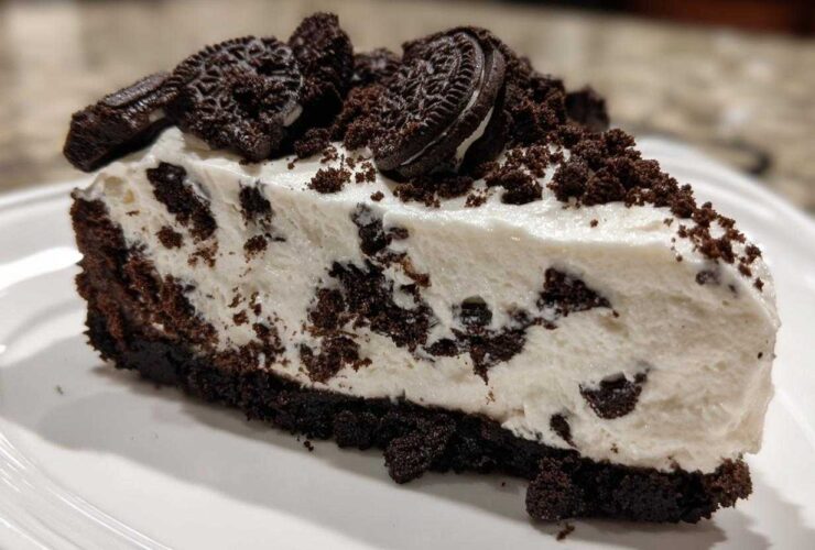 A thick slice of creamy, no-bake Oreo cheesecake featuring a dark chocolate crust and topped with crushed Oreos.