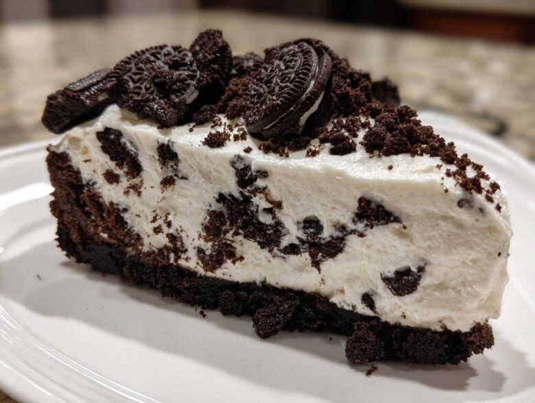 A thick slice of creamy, no-bake Oreo cheesecake featuring a dark chocolate crust and topped with crushed Oreos.