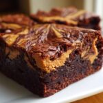 A close-up of a fudgy, dark chocolate peanut butter swirl brownies square on a white plate.