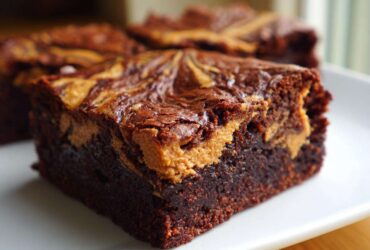 A close-up of a fudgy, dark chocolate peanut butter swirl brownies square on a white plate.