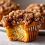 A close-up of a pecan pie muffin with a bite taken out, showing the moist interior and gooey brown sugar pecan topping.