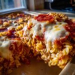 A close-up serving of baked pizza pasta casserole topped with melted mozzarella and pepperoni.