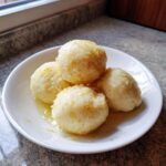 Four fluffy potato dumplings served in a white bowl, glistening with melted butter and sprinkled with toasted breadcrumbs.