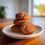 A stack of four soft, round pumpkin snickerdoodle cookies coated in cinnamon sugar, resting on a light plate.
