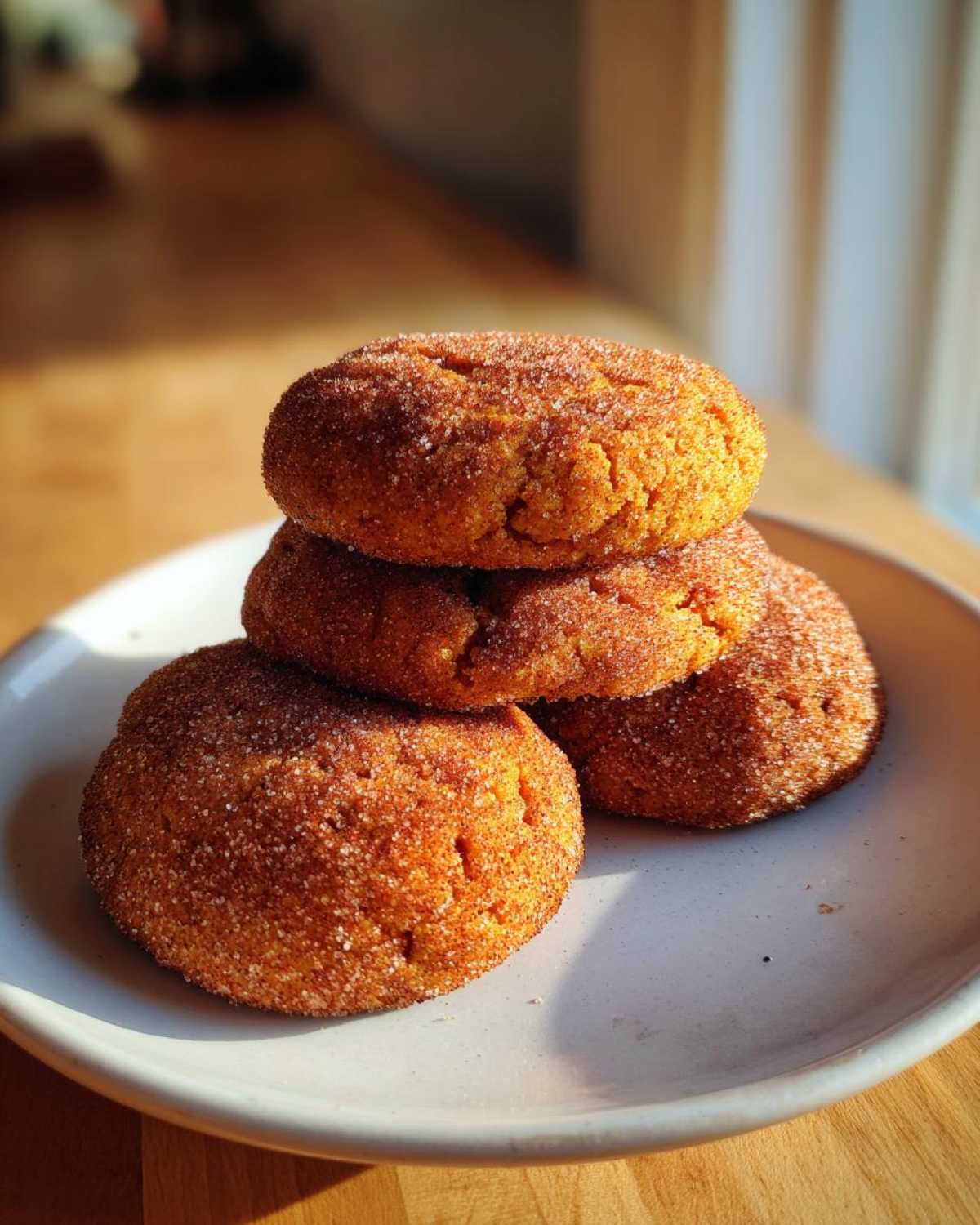 A stack of four soft, orange pumpkin snickerdoodle cookies coated heavily in cinnamon sugar, resting on a white plate.