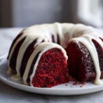 A slice cut from a rich, moist red velvet bundt cake topped with thick white cream cheese glaze.