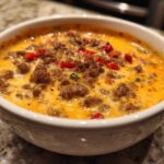Close-up of hot sausage cream cheese dip, bubbling with melted cheese and topped with diced red peppers.