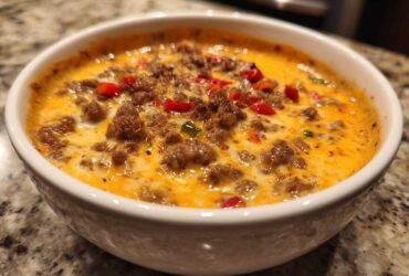 Close-up of hot sausage cream cheese dip, bubbling with melted cheese and topped with diced red peppers.