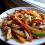 Close-up of seasoned chicken strips mixed with colorful bell peppers and onions for crockpot chicken fajitas.